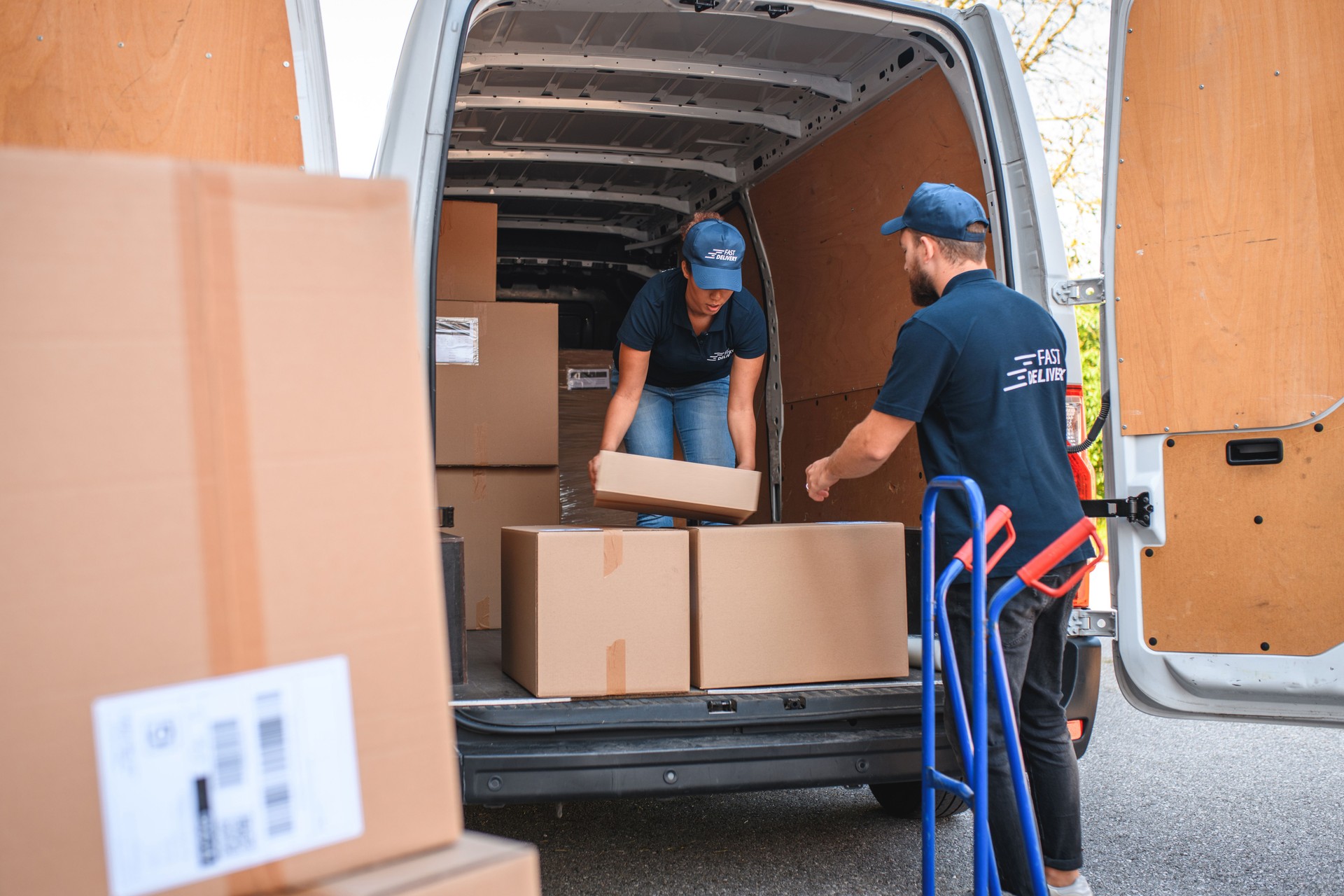 Young Delivery Woman And Man Controlling Packages In Cargo Space Of Van