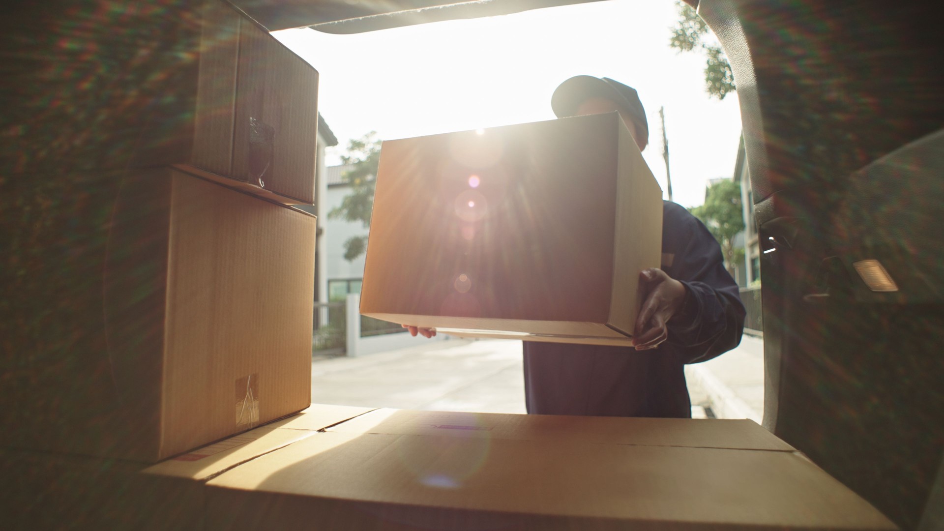 Delivery courier loading cardboard boxes packages into her car.